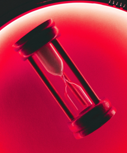 An hourglass sand timer is illuminated by red light.